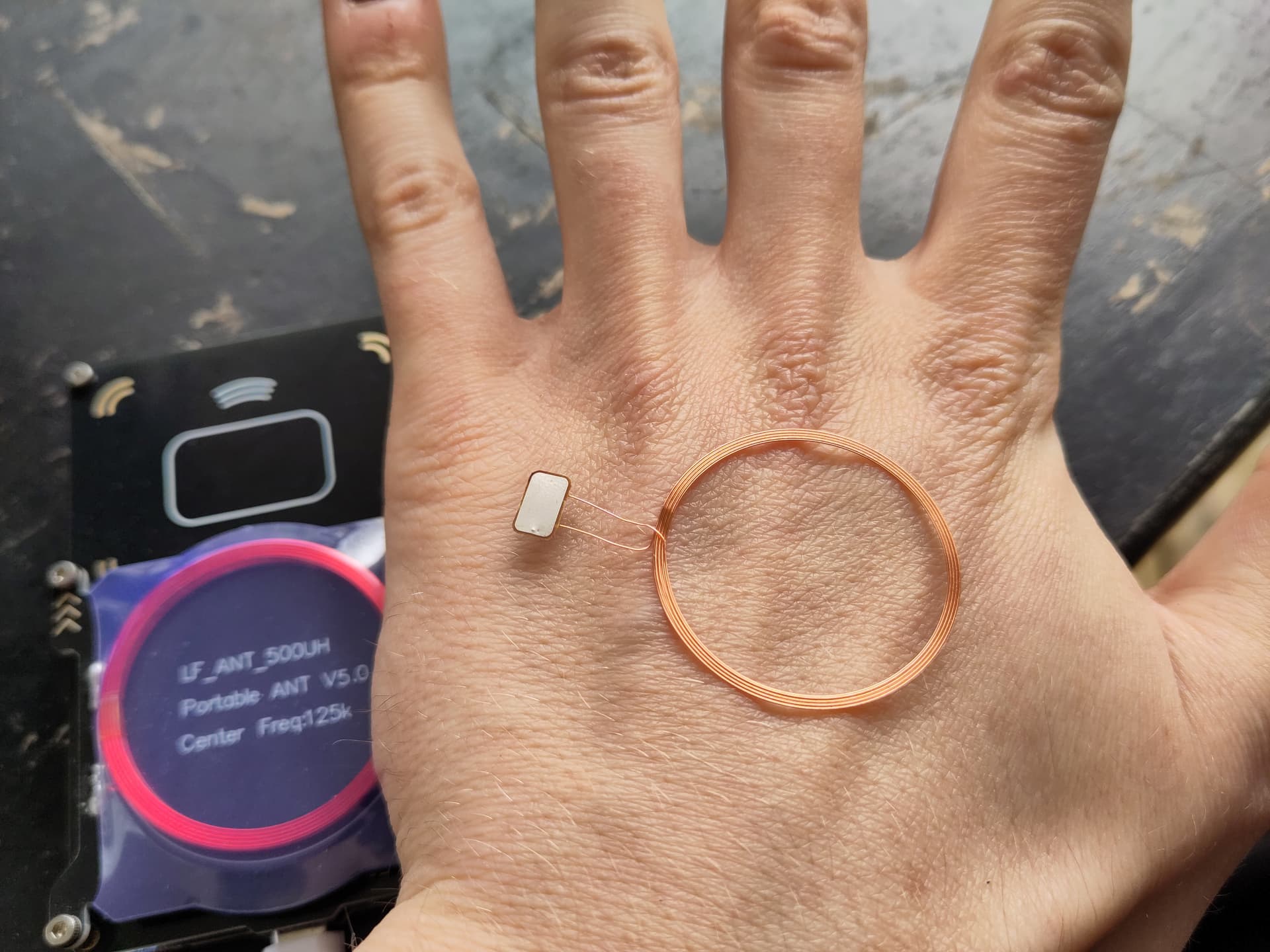 A chip connected to a large copper coil sitting on the back of Vvn's hand